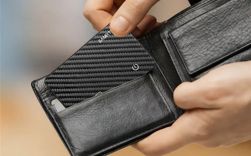 Ultra-slim iFindX wallet tracker card, compatible with Apple Find My network, being inserted into a leather bifold wallet.